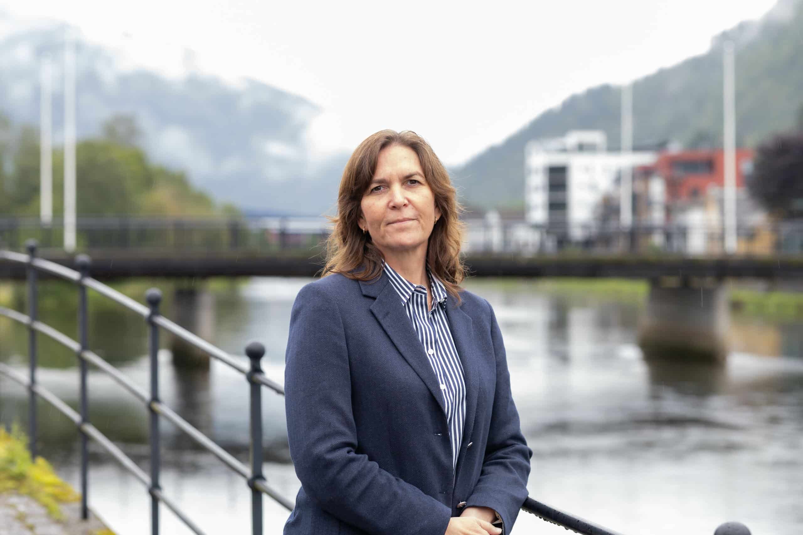 Bilde av Anya Therese Markhus, seniorrådgivar i Lotteritilsynet. Hun står ute ved elven i Førde, i en mørk dressjakke og en stripete skjorte.